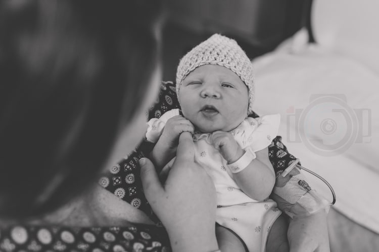 looking straight down at newborn baby girl picture over mother's shoulder eye contact adorable on hospital bed by danielle jacqueline photography in olive branch ms