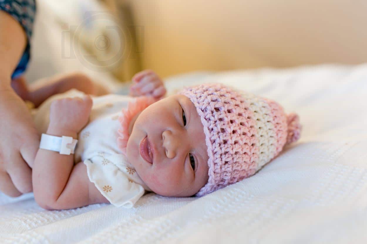 little baby newly born at hospital turning to left looking at camera while on bed wearing pink beanie super cute photographer near memphis tn