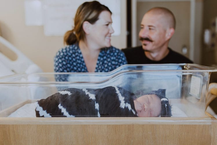 first time parents looking at each other in the eyes as their infant daughter sleeps in front of them giddy for successful delivery from pregnancy in olive branch ms captured by danielle jacqueline