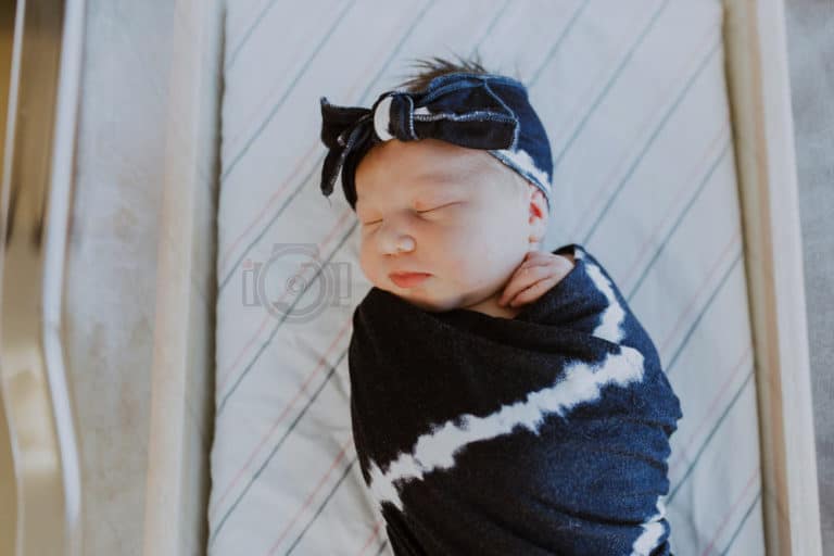 overhead portrait of newborn infant girl in dark blue blanket with stripes and matching bow for photography session with olive branch ms professional danielle jacqueline