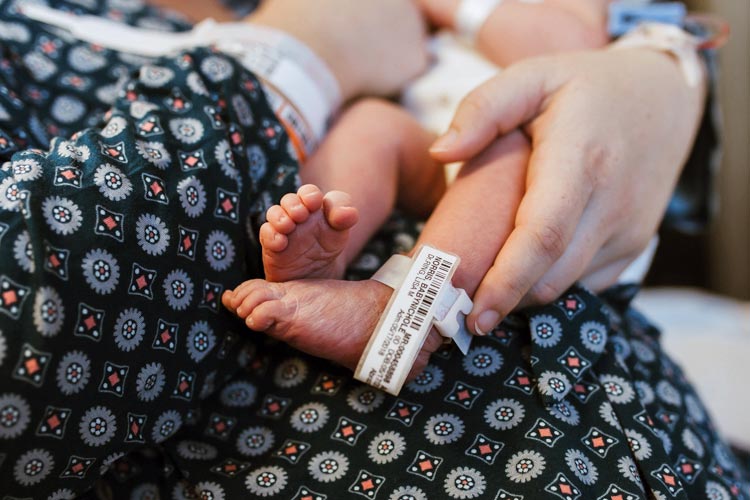 portrait of first time mother holding baby girl new arrival with hospital data on ankle for admission and ID in memphis tn