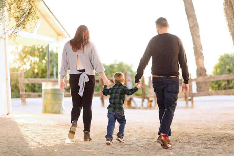 dad on right and mom of left child in middle holding hands walking away towards golden sun setting at farmhouse setting by desoto county ms family holidayphotographer danielle jacqueline