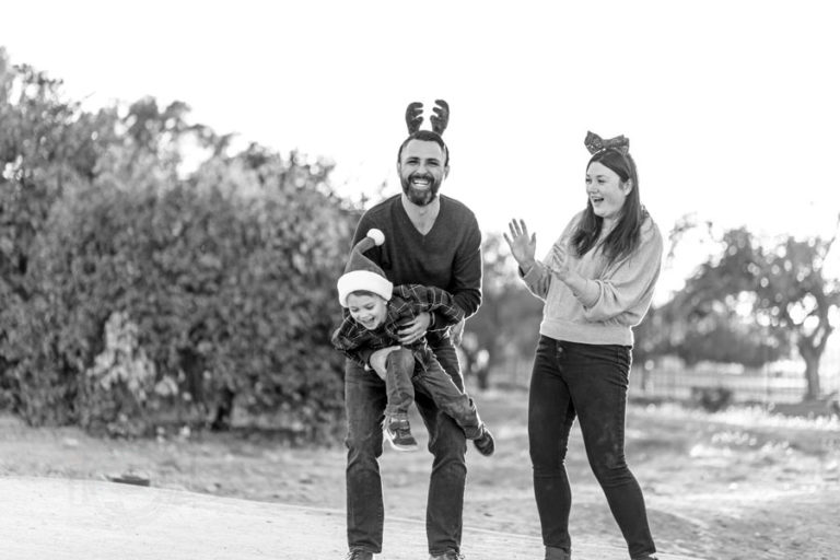 black and white photo of dad wearing reindeer headband and mom wearing mistletoe song being tickled in santa hat outdoors by danielle jacqueline photography from olive branch ms