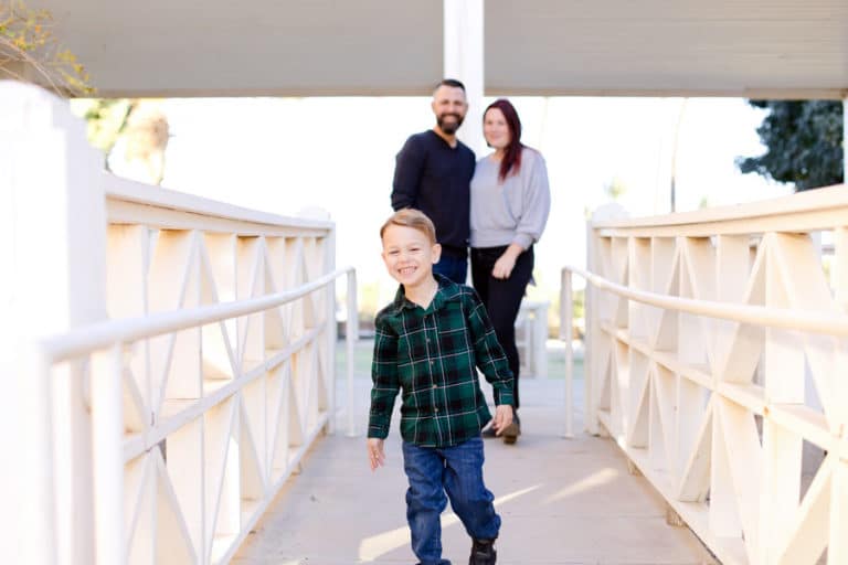 little boy walking away from both parents holding hands on bridge towards photographer eye level during holidays in 2020 memphis tn