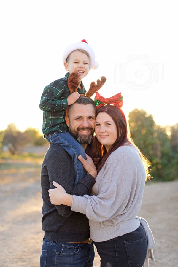 little boy sitting on father's shoulders wearing christmas hat for small family holiday pictures during golden hour with danielle jacqueline out of desoto county ms