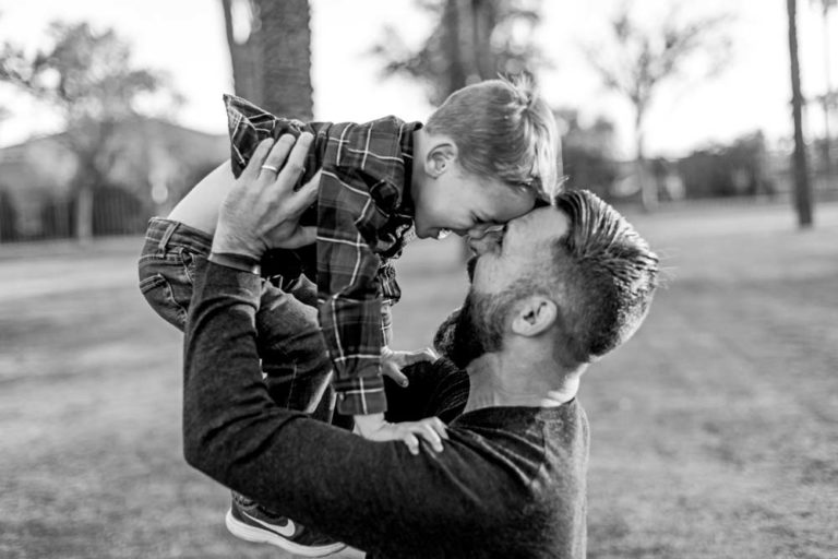 cute moment of son and father heads together eyes meet black and white as they laugh with park trees in background for family photography with danielle jacqueline in desoto county ms