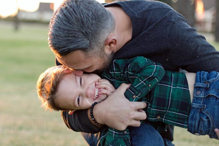 father holding son tight kissing him on the cheek as he grins big happy family photography for holidays by danielle jacqueline in desoto county ms