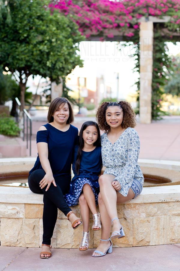 women of the family seated away from father and son as sun goes down in shade ledge of fountain at courtyard with big smiles on father's day with professional photographer