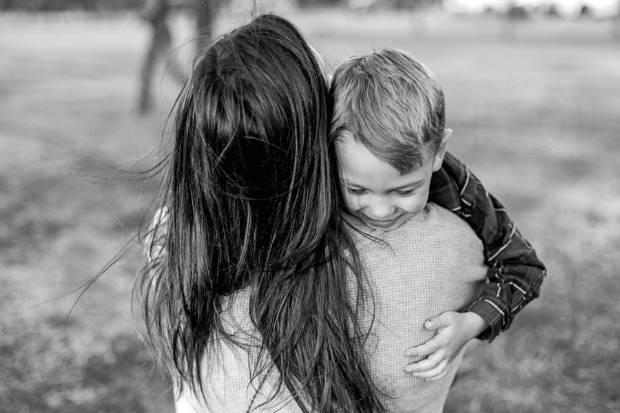 little boy holding his mom as she carries him away from photographer during session with danielle jacqueline worn out family before holidays black and white located in olive branch ms