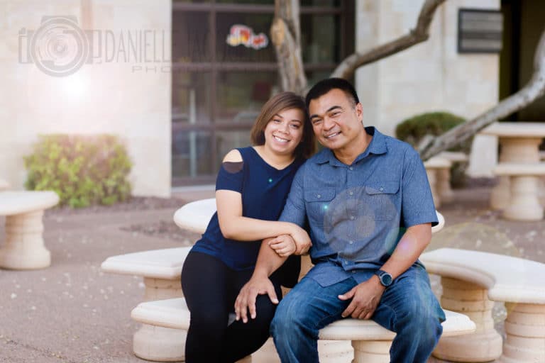 husband and wife seated on concrete picnic table in urban setting for father's day photography session with danielle jacqueline for entire family who's dad was serviceman living overseas