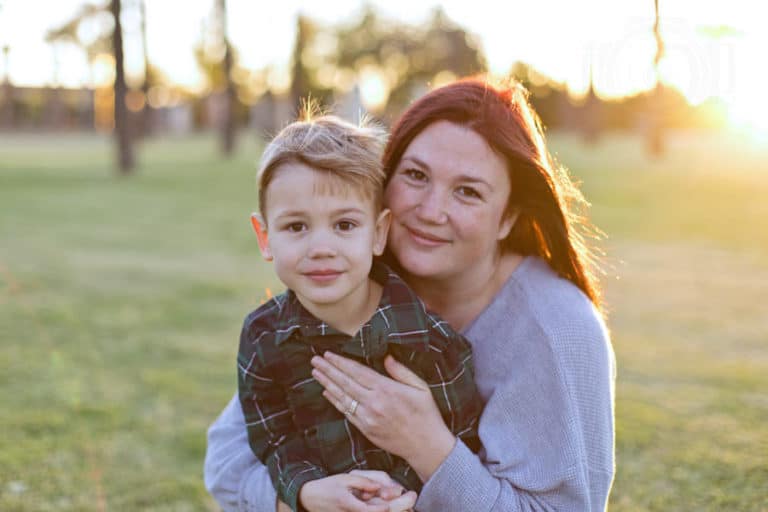 touching moment of mother with son at dusk in middle of grass field as she looks with serious look of love towards camera during holiday portrait session with memphis tn photographer danielle jacqueline