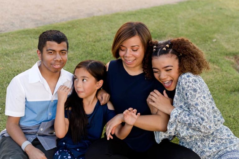 girls of family with special needs brother all hanging onto mommy while seated in grass during family photoshoot for father's day with danielle jacqueline photography in memphis area and olive branch ms