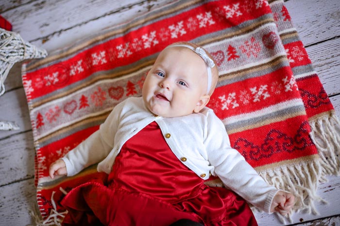 newborn baby first christmas portriats with theme red blanket dress and bow on hardwood floor by danielle jacqueline photography in olive branch ms serving southeast memphis