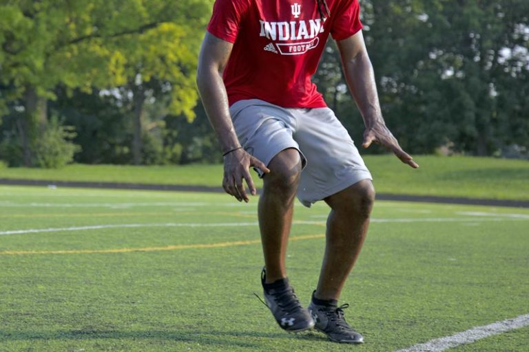 football player portrait in indiana university crimson t shirt with under armour cleats on doing drills in open field with painted lines during camp captured by danielle jacqueline photography out of olive branch ms