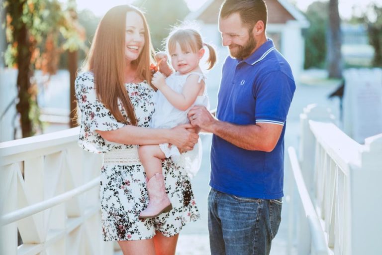 laughing parents enjoy photoshoot with danielle jacqueline photography on white bridge during golden hour for family portraits in olive branch mississippi