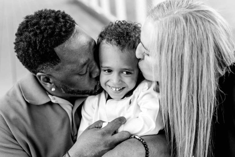 happy son of loving parents in the middle of two kisses curly hair squeeze family portrait black and white by danielle jacqueline in desoto county ms