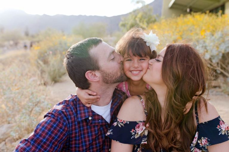 newly marries mom and dad kissing daughter on both chooks while outside with children's photographer danielle jacqueline