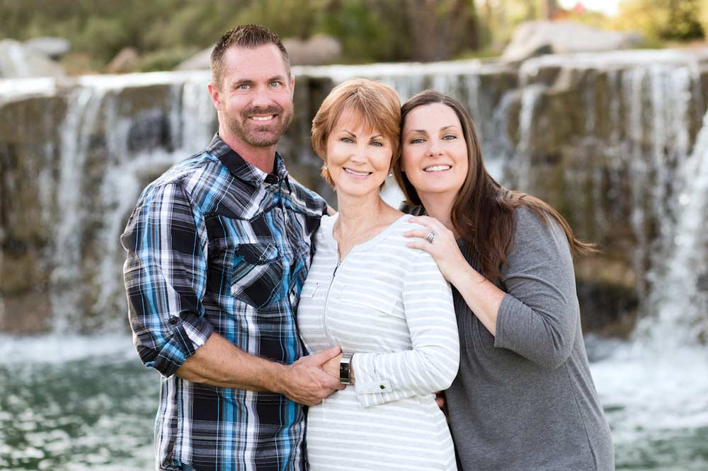 grandmother to be be standing in between parents of next generation family members portraits waterfall from river in background by desoto county photographer danielle jacqueline