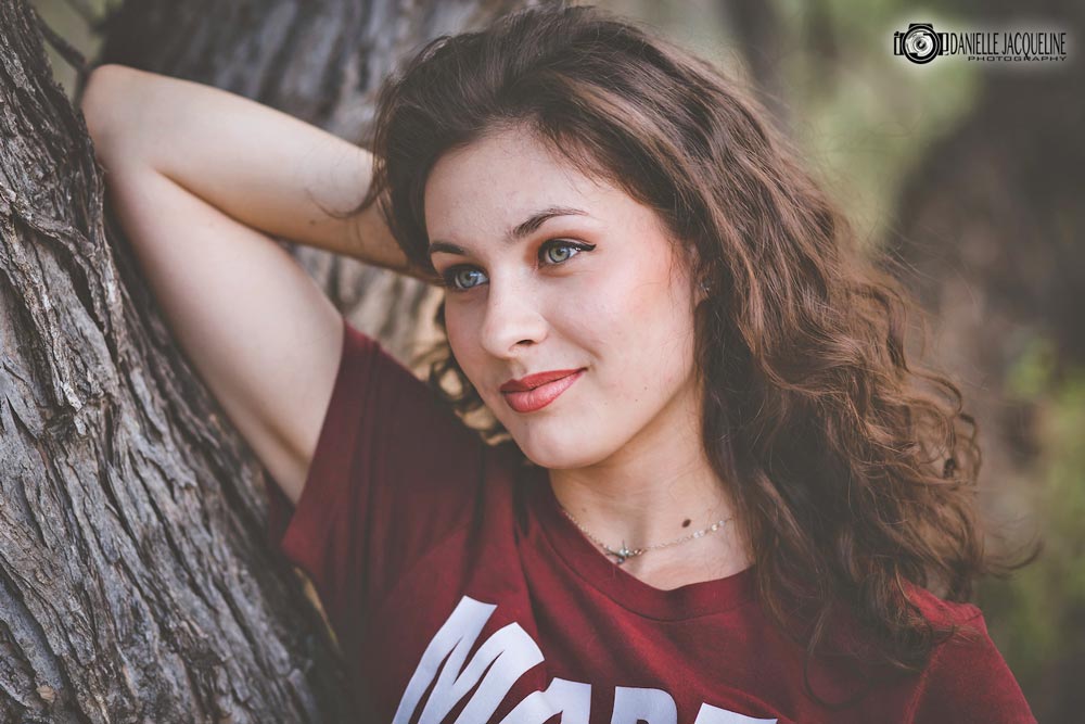 brunette burgandy shirt arm over head next to tree thinking of smiling during senior portrait session natural settings in olive branch mississippi by danielle jacqueline professional