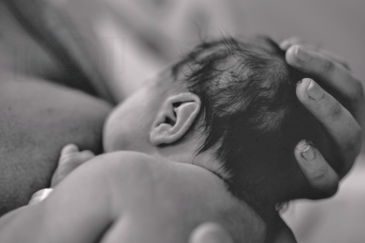 mother cupping the back of baby boy's head in delivery room as he feeds naturally for black and white portrait by danielle jacqueline photography in olive branch ms