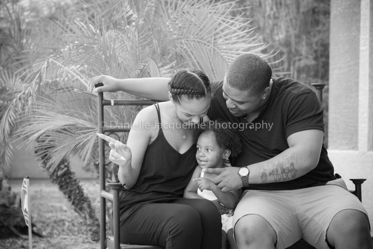 young family portraits sitting on bench teaching cute infant daughter to look and listen at guidance while sitting on bench father arm over wife child in the middle adorable setting by desoto county ms photographer danielle jacqueline