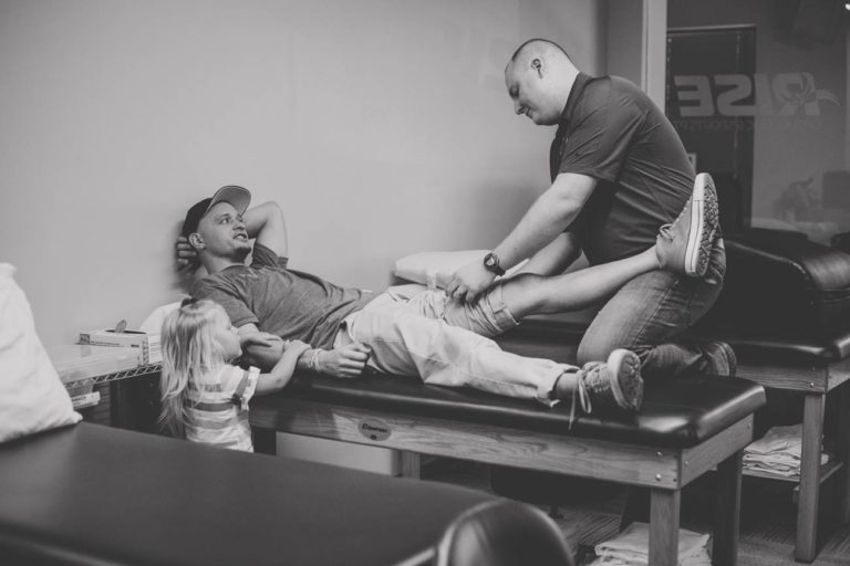 picture of physical therapy patient talking to certified pt about knee pain with toddler daughter holding hand at family clinic caught on camera by olive branch business photographer danielle jacqueline black and white candid moment