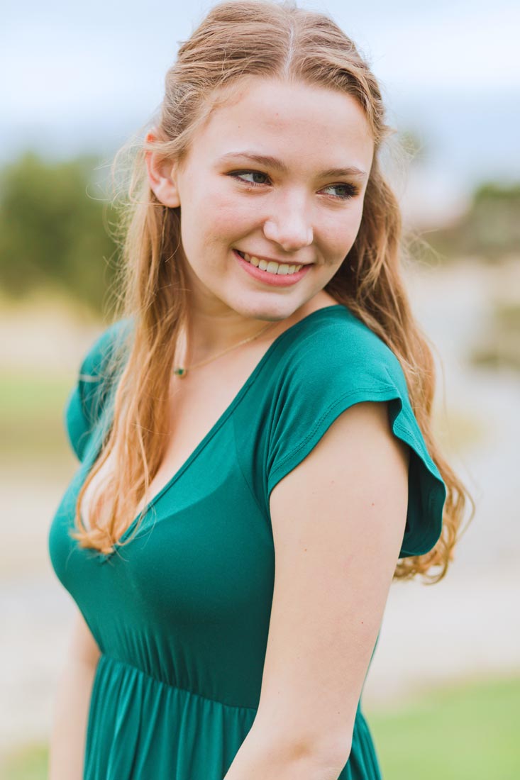 green dress red hair smiling off to the left during outdoor high school senior photo session with danielle jacqueline now in olive branch ms