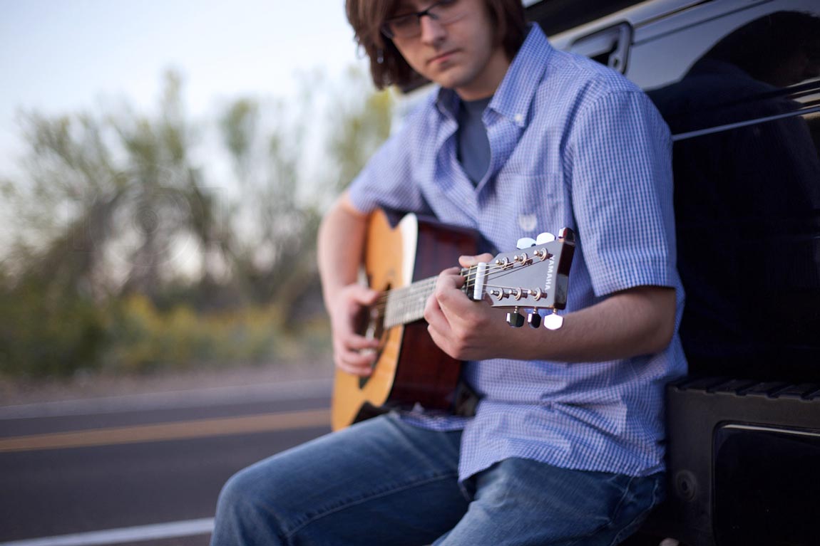 strumming on the guitar on the back of his truck on the side of the road long haired boy in glasses and blue senior photos by danielle jacqueline mississippi memphis area