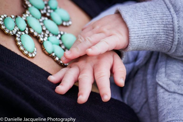 new baby arrival stretching out fingers while mommy is holding him outside colorful necklace sweatshirt fall weather after pregnancy photo by danielle jacqueline in olive branch ms