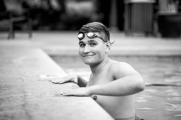 hands on ledge of pool young man child of proud parents high school swimming team for child graduation photos with danielle jacqueline