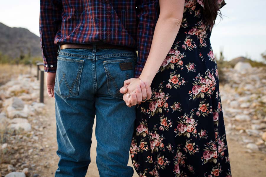 happily married couple standing outside looking away from camera holding hands tightly photographing their waste matching shirt to wife's dress flowers dry setting family portrait by danielle jacqueline