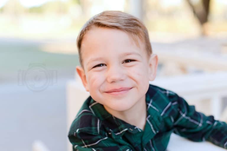 young boy huge grin outdoor family photos with kids pictures by danielle jacqueline photography wearing green and blue flannel in front of natural park setting in collierville tn