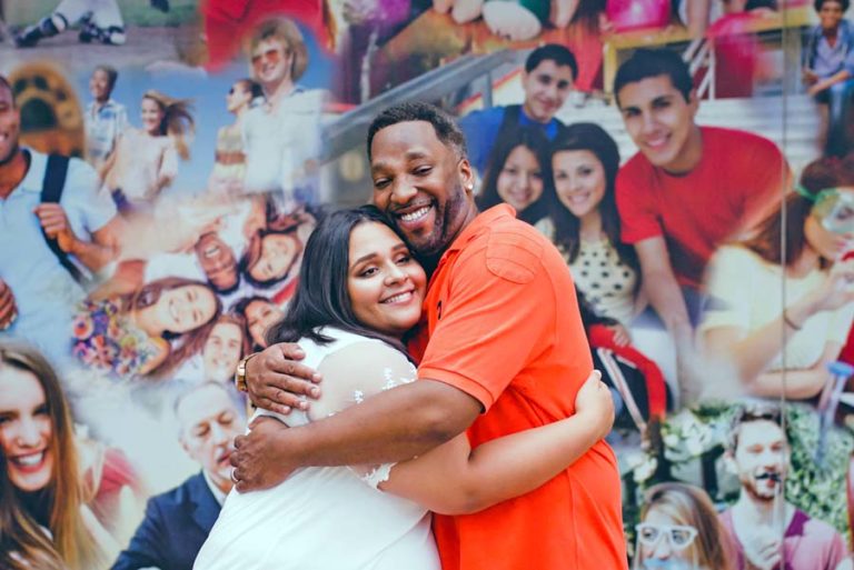 city walk photo shoot with danielle jacqueline photography services with father in orange polo hugging sister in law in front of huge wall collage painted with multitude of people from memphis tn for family photos