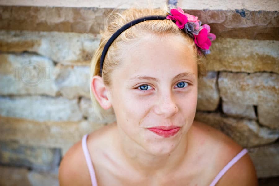 pre teen middle school pictures of blonde with pink bow in hair closed mouth grin in front of stone wall leaning tank top for proud parents in southaven mississippi by danielle jacqueline photography