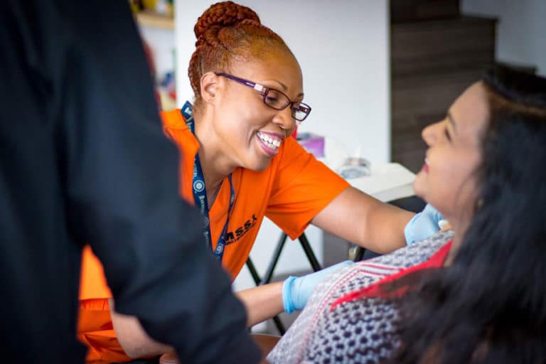 smiling business owner orange company outfit braided hair bun glasses removing mole of client for mobile skin screening services in memphis tn photography by danielle jacqueline in person view