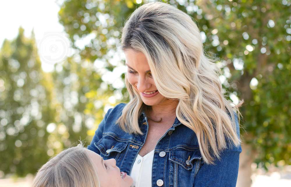 pretty hair mother blonde looking down at young daughter staring up at her jean jacket sun light in background through mississippi trees during beautiful day for photographer session with danielle memphis