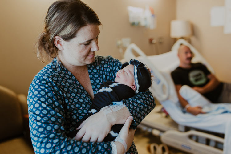 mom adoring her daughter in blue bow swaddled while daddy awaits them on bed creative fresh 48 ideas by danielle jacqueline photography in desoto county ms