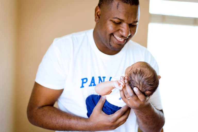 super happy daddy holding healthy baby son panama representing white shirt at in home photoshoot professional newborn photography services in south memphis tn area by danielle jacqueline out of olive branch