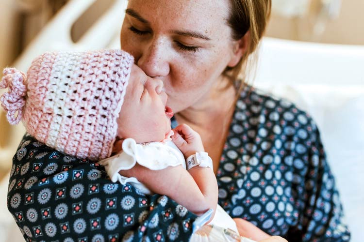 big smooches from mommy for new arrival baby girl pink beanie hospital bracelet in bed during fresh 48 session with danielle jacqueline in olive branch ms