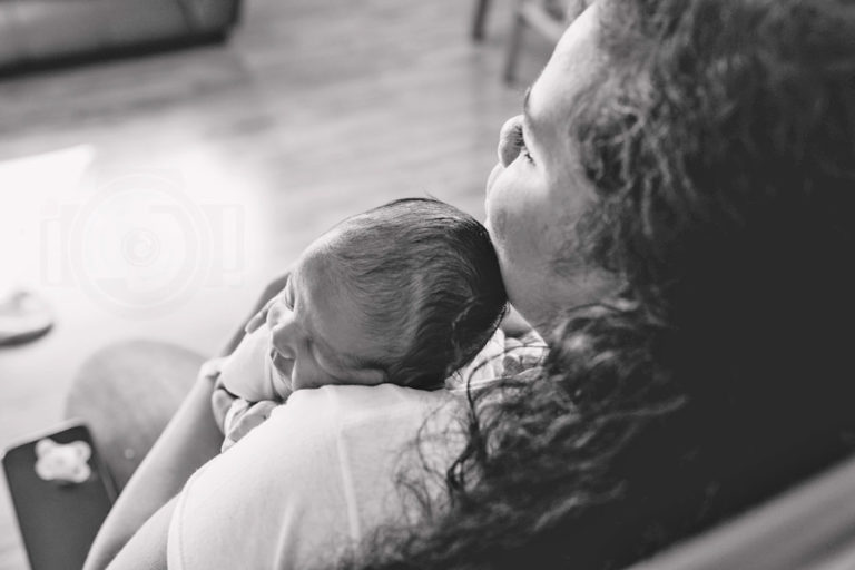 downward angle towards mother's shoulder in hospital room after baby delivery holding newborn son against shoulder for black and white image with parents by danielle jacqueline services in olive branch ms