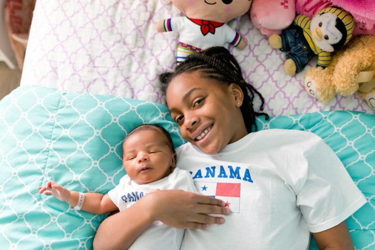 smiling big sister in braids of panama immigrant parents laying down with little baby brother in new world of girls room style with teal and stuffed animals for kids portraits with danielle jacqueline in germantown tn