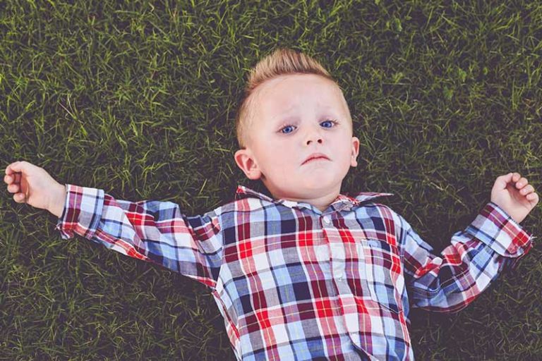 little boy in plaid long sleeves not happy about taking pictures with parents and danielle jacqueline children's photographer laying in grass exhausted ready to go back to mississippi home