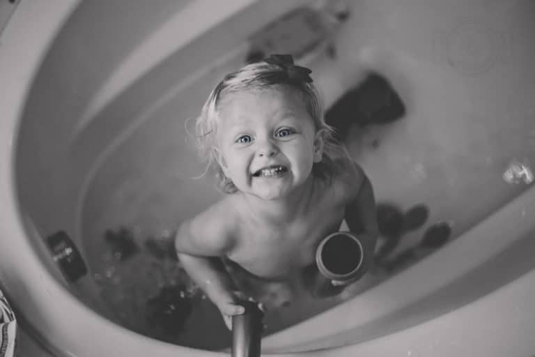 playing daughter black and white portrait during bath time with toys big tub huge cheese smile bow in hair for parents of olive branch ms residents with danielle jacqueline's children's photographer services