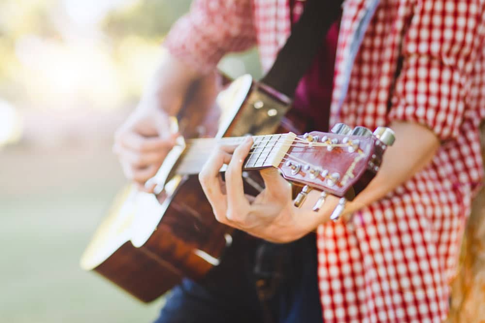 close up of high school graduate playing guitar strings in natural setting outdoors with red and white checkered dress shirt and jeans by danielle jacqueline photography quotes page olive branch mississippi memphis area