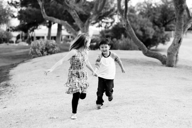 older sister in sun dress and black tights pulling little brothers arm as they bolt through the open grass for sibling photoshoot with danielle jacqueline in desoto county mississippi