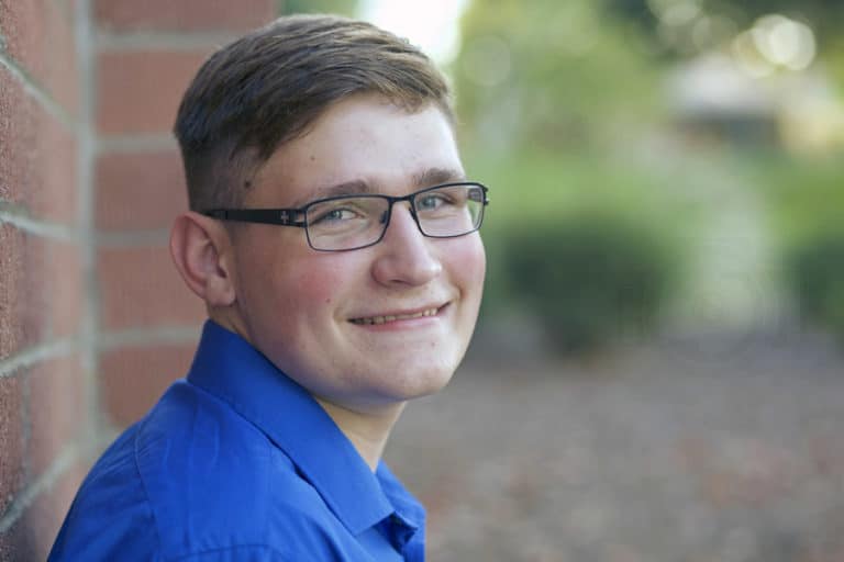 smiling groomed look for high school graduating senior boy in blue polo leaning against wall with danielle jacqueline