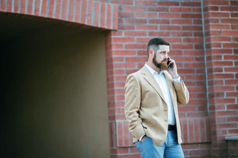 business man in blazer and jeans bearded haircut talking on phone in front of brick laid tunnel outside of company's office building lifestyle images for ceos by danielle jacqueline photography in olive branch ms