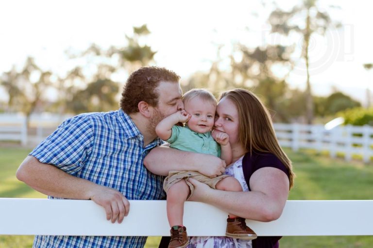 adorable mother father baby boy photo shoot on the farm sitting on white picket fence rural area of desoto county ms pasture smothering son with love during golden hour dusk by danielle jacqueline in color