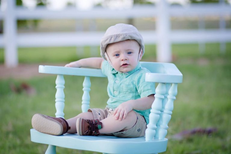 adorable infant seated on turquoise wooden stool in matching shirt at farmhouse setting in oxford mississippi for family photos with baby by danielle jacqueline