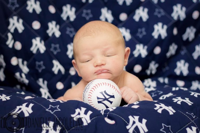 newborn baby photo shoot in olive branch ms with new york yankees quilt and baseball under baby's chin eyes barely open almost asleep soft skin danielle jacqueline photography